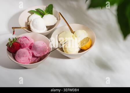 Helle Gourmet-Komposition mit drei Schüsseln Eis in verschiedenen Geschmacksrichtungen: Erdbeere mit frischem Obst, Vanille oder Kokos mit Minzblättern, Stockfoto