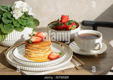 Einladende Frühstückskomposition mit einem Stapel goldener Pfannkuchen mit frischen Erdbeeren und Sirup, serviert auf einem weißen Teller Stockfoto