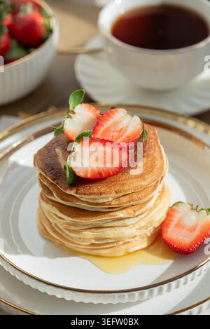 Einladende Frühstückskomposition mit einem Stapel goldener Pfannkuchen mit frischen Erdbeeren und Sirup, serviert auf einem weißen Teller Stockfoto