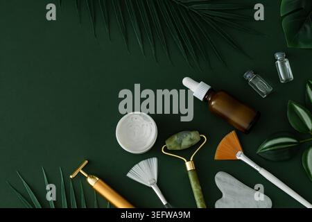 Luxuriöse natürliche Hautpflege-Komposition mit Beauty-Accessoires, Beauty-Creme, Jaderoller, Serumflasche und tropischen Blättern auf grünem Hintergrund. Stockfoto