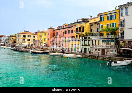 Peschiera del Garda, Italien - 30. April 2026: Farbenfrohe Gebäude entlang der Uferpromenade in Peschiera del Garda, mit Booten im klaren Türkis Stockfoto