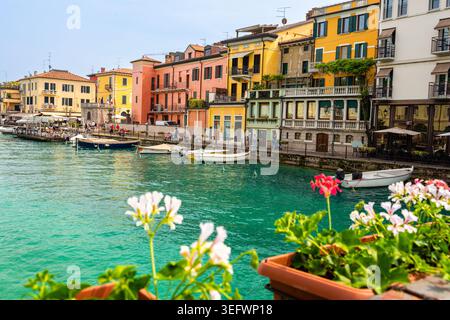 Peschiera del Garda, Italien - 30. April 2026: Lebhafte Gebäude säumen den Kanal in Peschiera del Garda, Italien, mit angedockten Booten und Blumen in Töpfen Stockfoto