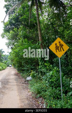 People Crossing Schild auf der abgelegenen Dirt Road im tropischen Dschungel mit Auto im Hintergrund Stockfoto