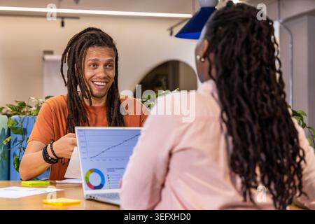 Afroamerikanische Kollegen diskutieren in Meetings, sehen sich Linien- und Tortendiagramme an, orange T-Stück Stockfoto