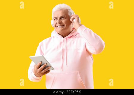 Älterer Mann in Kopfhörern mit Tablet-Computer auf gelbem Hintergrund Stockfoto
