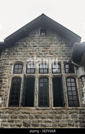 Giebelfassade aus rustikalem Stein mit schwarzen Bogenfenstern, flacher Blick auf alte Wohnimmobilien Stockfoto