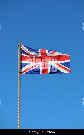 Die Nationalflagge des Vereinigten Königreichs winkt auf einem Fahnenmast vor einem klaren blauen Himmel Stockfoto