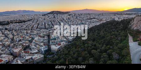 Ein weites Panorama-Luftbild zeigt die dichte Zersiedelung von Athen, Griechenland, neben dem üppigen Grün des Lycabettus-Hügels, während die Sonne aufgeht Stockfoto