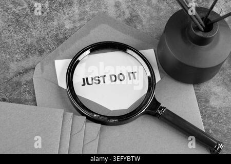 Eine Lupe auf einem Schreibtisch hebt ein weißes Papier hervor, das den fetten Satz JUST DO IT zeigt. Stockfoto