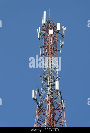 Telekommunikations-Gitterturm mit mehreren Paneelantennen und Funkgeräten auf einem rot-silbernen Stahlmast, vor einem klaren blauen Himmel in hellem d Stockfoto