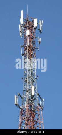 Rot-weißes Gitter-Telekommunikationsmast mit mehreren Sektorantennen steht hoch unter einem klaren blauen Himmel und überträgt moderne Kabel Stockfoto