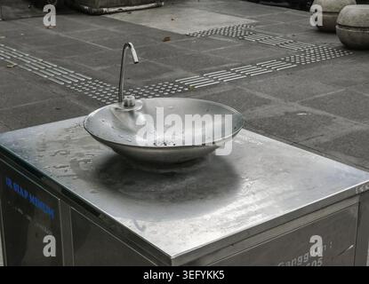Trinkwasserbrunnen aus Edelstahl auf einem gepflasterten Bürgersteig in einer Stadt in Indonesien. Öffentliche Armatur im Freien mit rundem Becken und Stockfoto