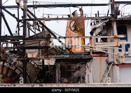 Yilan, Taiwan - 31. März 2025: Feuerhädigter Trawler in Nanfangao mit verkohltem Aufbau, verbrannten Rahmen und rostigen Netzrollen entlang des Rumpfes. Stockfoto