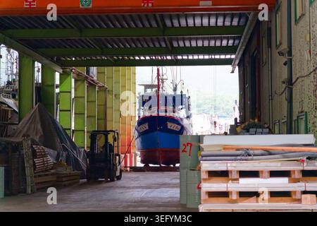Yilan, Taiwan - 31. März 2025: Fischereifahrzeug am Eingang der Nanfangao Werft mit einem Deckenkran und Gabelstapler in der Industrieanlage. Stockfoto
