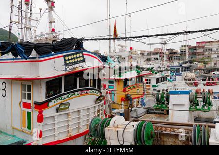 Yilan, Taiwan - 31. März 2025: Bunte Fischereifahrzeuge überfüllten sich im Hafen von Nanfangao, mit kunstvollen Rumpfdekorationen und hinter ihnen sichtbaren städtischen Gebäuden. Stockfoto