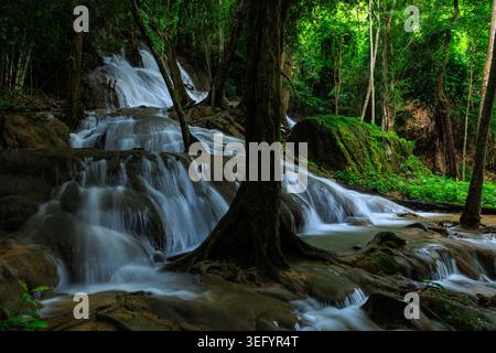 Ein mehrstufiger Wasserfall fällt über moosige Felsformationen in einem dichten, üppigen tropischen Regenwald, perfekt für Natur- und Reisethemen. Stockfoto