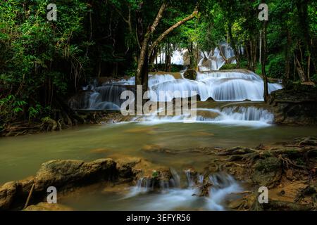 Ein malerischer gestufter Wasserfall fließt über Natursteinformationen in einem üppigen, lebhaften tropischen Regenwald. Stockfoto