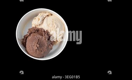 Zwei Kugeln Eis werden in eine Schüssel gegeben. Ein Löffel ist Schokolade und der andere ist Vanille. Die Schüssel befindet sich auf einer schwarzen Oberfläche, wodurch die hervorgehoben wird Stockfoto