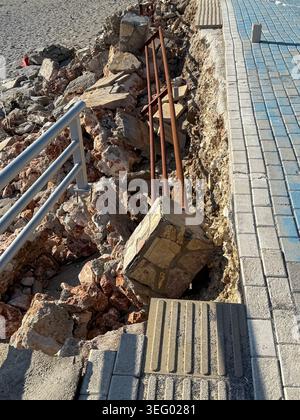 Beschädigter Bürgersteig und Betonschutt mit freiliegendem Bewehrungsstahl im urbanen Hintergrund. Mobiles Foto Stockfoto
