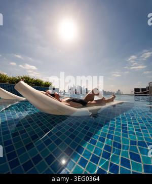 Frau schwimmt im Infinity-Pool mit Blick auf die Skyline von dubai Stockfoto