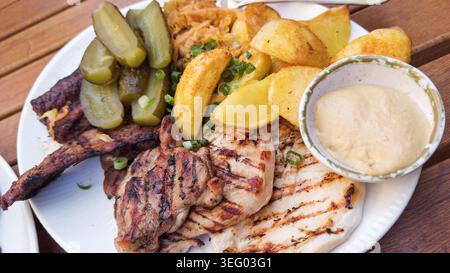 Gegrillte Fleischplatte mit Kartoffeln, Gurken und Sauce Stockfoto