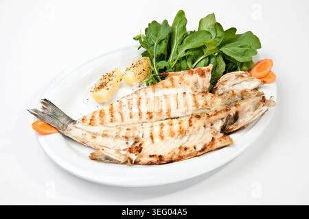 Gegrillter Wolfsbarsch auf einem Teller serviert, ganzer frischer Fisch mit knuspriger Haut und rauchig verkohlter Oberfläche, traditionelle mediterrane Meeresfrüchte-Küche Stockfoto