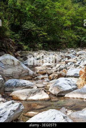 Sanzhanxi Flusstal in Hualien, Taiwan. Große graue Felsbrocken säumen einen flachen Bach. Üppig grüner Wald bedeckt den Hintergrund der Berge. Stockfoto