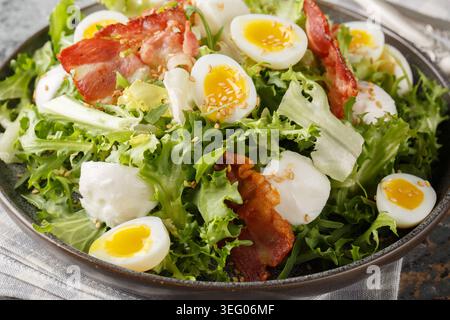 Frischer Salat aus weich gekochten Wachteleiern, Speck, Mozzarella, Sesamsamen und gemischten Salatblättern in Nahaufnahme auf einem Teller auf dem Tisch. Horizontal Stockfoto