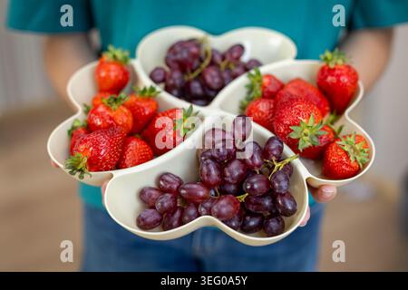 Frische Erdbeeren Und Trauben Im Obsttablett. Person hält ein geteiltes Tablett gefüllt mit Reifen Erdbeeren und roten Trauben für gesunde Ernährung, Party Stockfoto