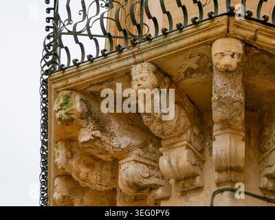 Nahaufnahme eines schönen historischen barocken Steinbalkons mit kunstvoll geschnitzten Gesichtern, mythischen Figuren und einem dunklen schmiedeeisernen Geländer in Europa Stockfoto