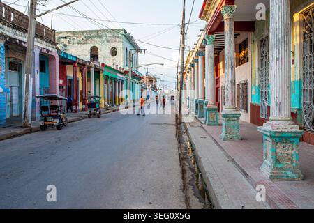 Eine lebhafte Straße in Trinidad zeigt kubanische Kolonialarchitektur mit Veranden, die von klassischen Säulen geschmückt sind. Die Szene fängt das lokale tägliche Leben mit ein Stockfoto