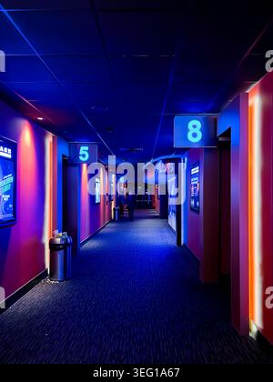 Blick auf einen Flur in einem Multiplex-Kino, das zu den Bildschirmen führt, dunkel, aber mit stimmungsvollem, atmosphärischem blauem Licht beleuchtet Stockfoto