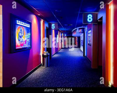 Blick auf einen Flur in einem Multiplex-Kino, das zu den Bildschirmen führt, dunkel, aber mit stimmungsvollem, atmosphärischem blauem Licht beleuchtet Stockfoto