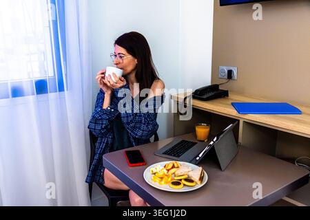 Frau, die während ihrer morgendlichen Routine mit Frühstück aus der Ferne arbeitet Stockfoto