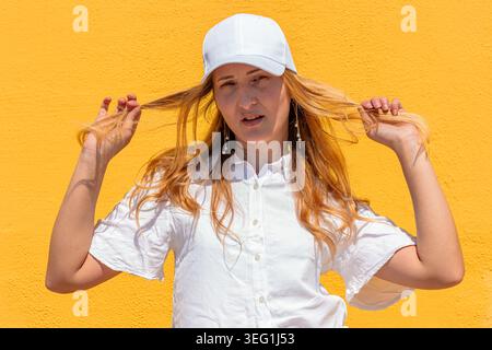 Junge Frau, die Haare zieht, weiße Baseballmütze trägt Stockfoto
