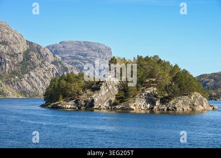 Eine kleine felsige Insel mit grünen Kiefern und einem winzigen weißen Leuchtturm mit einem roten Dach in einem norwegischen Fjord. Stockfoto