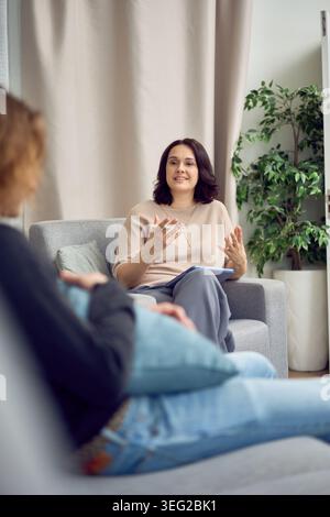 Eine freundliche Beraterin gibt mit beiden Händen Gesten, während sie ihrem Klienten während einer erfolgreichen Therapiesitzung in einer sonnendurchfluteten Moderne ein Konzept erklärt Stockfoto