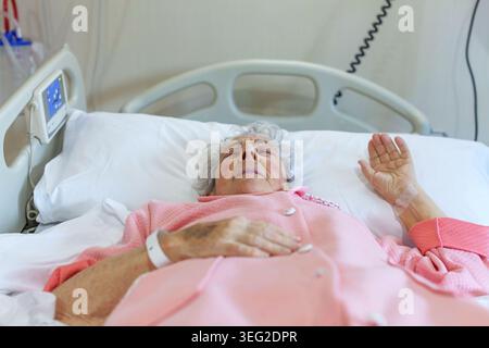 Eine ältere Patientin liegt bequem in einem Krankenhausbett und wird medizinisch versorgt. Sie scheint sich friedlich auszuruhen und hebt das Gesundheitswesen hervor Stockfoto
