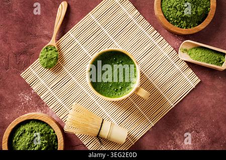 Blick von oben auf schäumenden zeremoniellen Matcha-Tee mit lebendigem grünem Matcha-Pulver, Bambus-Schneebesen und Schaufel auf einer Wabi-Sabi-Matte, wodurch ein ruhiger Zen-Superfoo entsteht Stockfoto