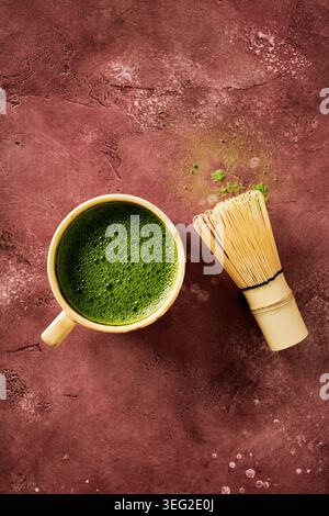 Blick von oben auf zeremoniellen Matcha-Tee in einer rustikalen Tasse neben einem Bambus-Schneebesen auf einer strukturierten Oberfläche, minimalistische Zen-Ästhetik mit Wabi-Sabi-Stimmung und Stockfoto