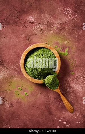 Zeremonielles Matcha-Pulver in einer Holzschale und einem Löffel auf rustikalem Steinhintergrund, minimalistische Zen-Ästhetik mit Wabi-Sabi-Textur. Leuchtendes Grün Stockfoto