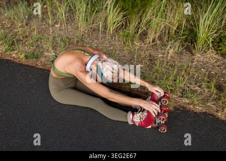 Eine Frau in Sportkleidung dehnt sich auf einem asphaltierten Weg, trägt Rollschuhe. Umgeben von der Natur in Australien bereitet sie sich auf eine Skating-Session unter vor Stockfoto