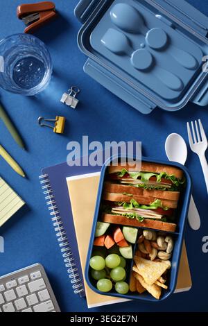 Eine blaue bento-Box gefüllt mit einer nahrhaften Mahlzeit aus Sandwiches, frischen Trauben, Karottenstäbchen, Nüssen und Crackern, perfekt für einen gesunden Lebensstil oder für Offi Stockfoto