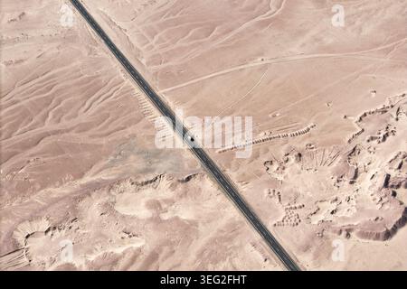 Aus der Vogelperspektive auf eine lange asphaltierte Autobahn, die durch die Atacama-Wüste in Chile führt, mit Sanddünen und kargem Gelände. Abgelegene landschaftlich reizvolle Roadtrip-Landschaft u Stockfoto