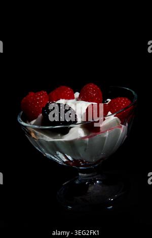 Köstliches Dessert mit frischen Himbeeren und brombeere auf weißer Creme in einer Glasschale isoliert auf schwarzem Hintergrund Stockfoto