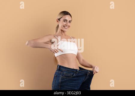 Lächelnde junge Frau in übergroßen Jeans mit schmaler Taille nach Gewichtsverlust Stockfoto