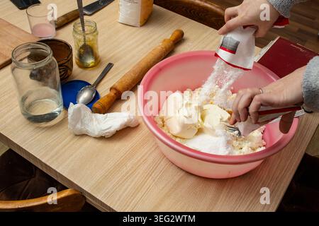 Frau poriert Puderzucker auf Käsekuchen, in einer rosafarbenen Plastikschale, authentische osterwaren Stockfoto