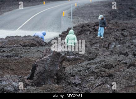 Familie mit Kind, die auf den erstarrten Lavaflüssen in der Nähe von Grindavik, Island, Europa mit einer gesperrten Straße im Hintergrund spaziert Stockfoto