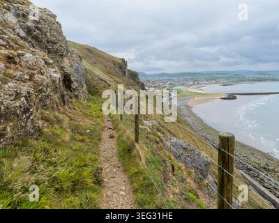 Der unbefestigte Pfad schlängelt sich entlang der steilen Great Orme Klippe und bietet einen weiten Blick auf die Stadt Llandudno, den West Shore Beach und das Meer an einem bewölkten Tag im Norden Stockfoto