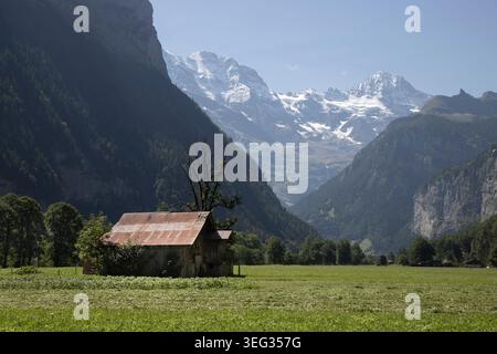 Rustikale Scheune auf grüner Wiese mit hoch aufragenden schneebedeckten schweizer alpen im Hintergrund Stockfoto